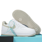 A pair of Nike Air Force 1 Low sneakers in white with beige heel accents and a mint green shoelace, displayed on a light blue box. One shoe is shown in profile, and the other is positioned behind it to display the sole.