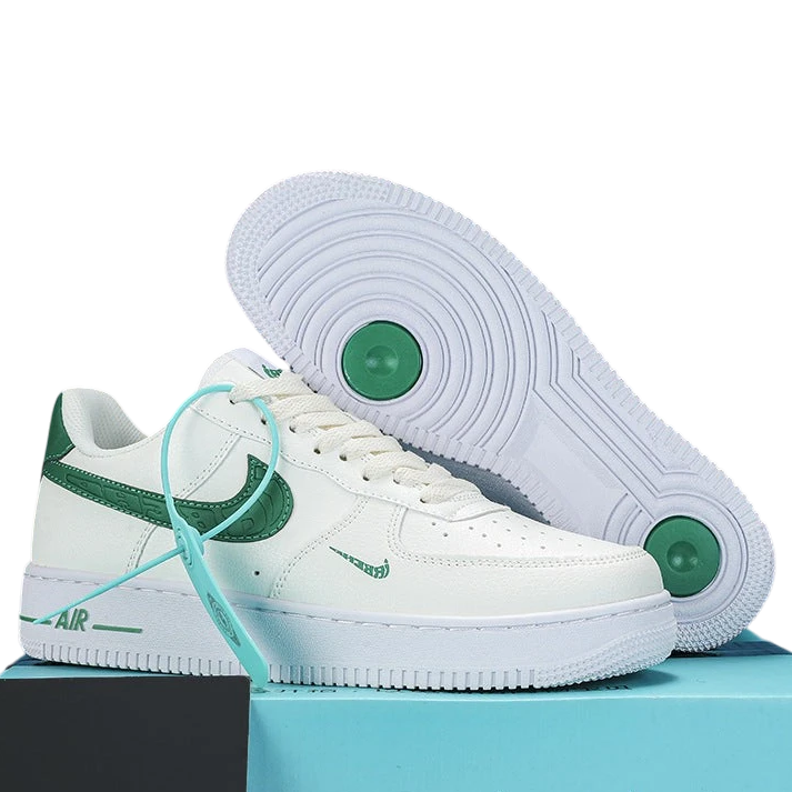 A pair of white low-top sneakers with green accents, including a green Swoosh on the side, a green heel tab, and a light blue tie detail, displayed on a light blue box with a black block. The outsole of one shoe is shown propped up behind the other.